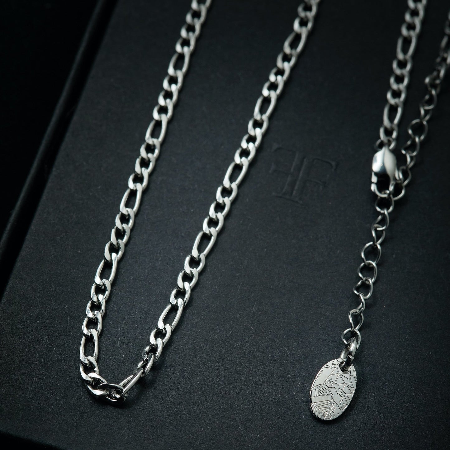 Men's silver figaro layering chain on packaging box