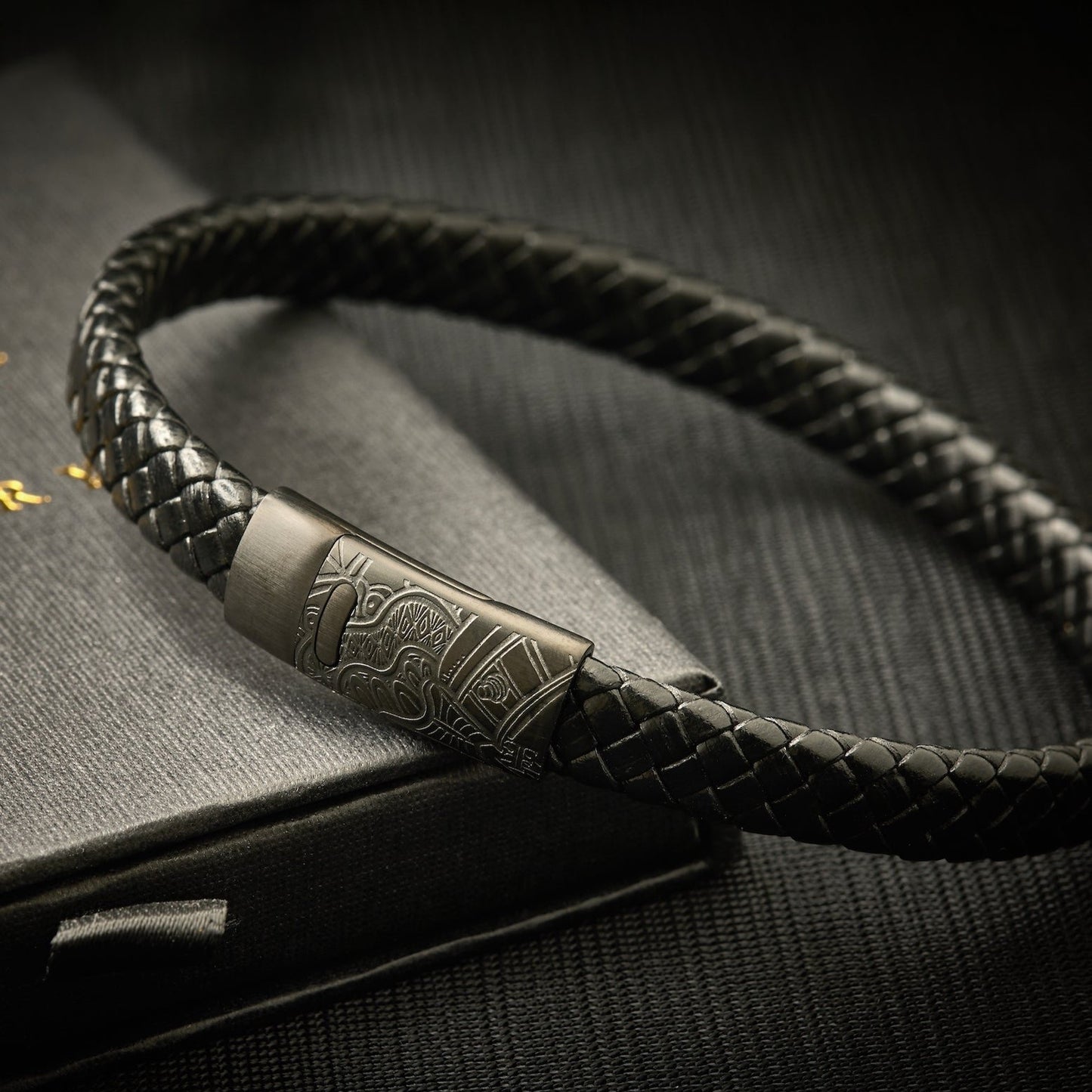 Men's artist-engraved twisted leather bracelet with black clasp on packaging box