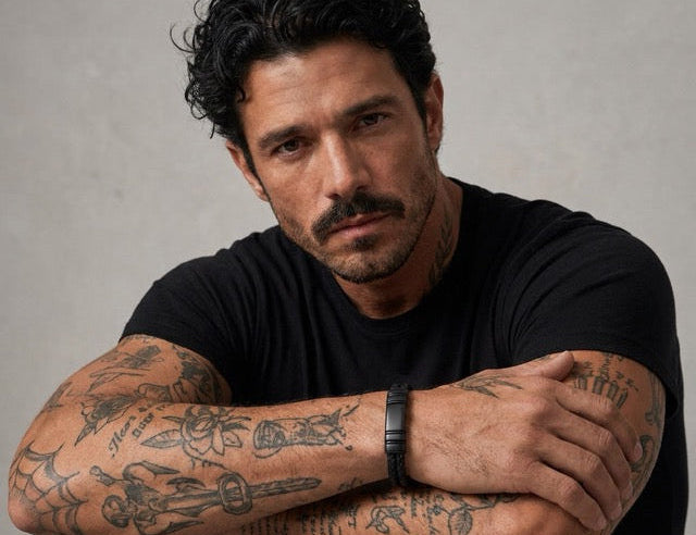 Man with tattoos on his arms wearing a black shirt against a gray background