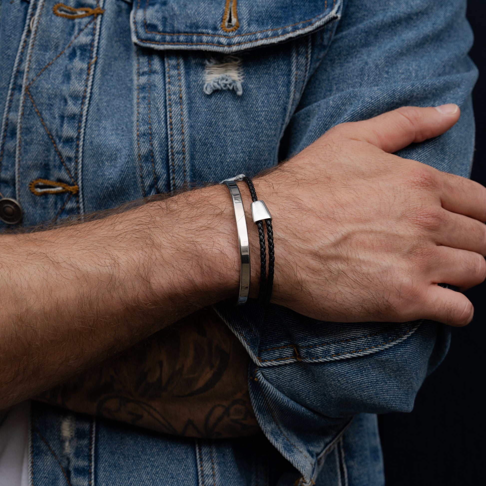 Close-up of a person wearing multiple leather and titanium bracelets on a denim background