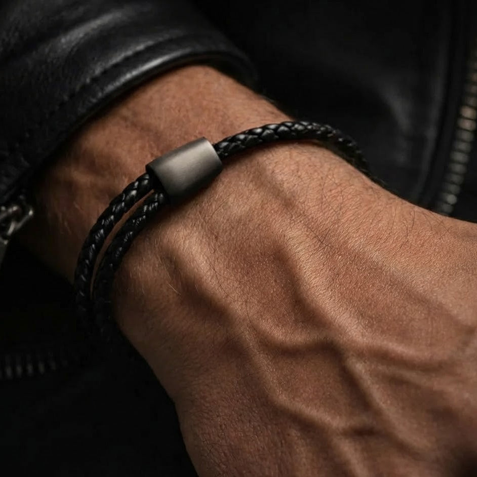 Close-up of a wrist wearing a black braided leather bracelet with a metallic clasp.